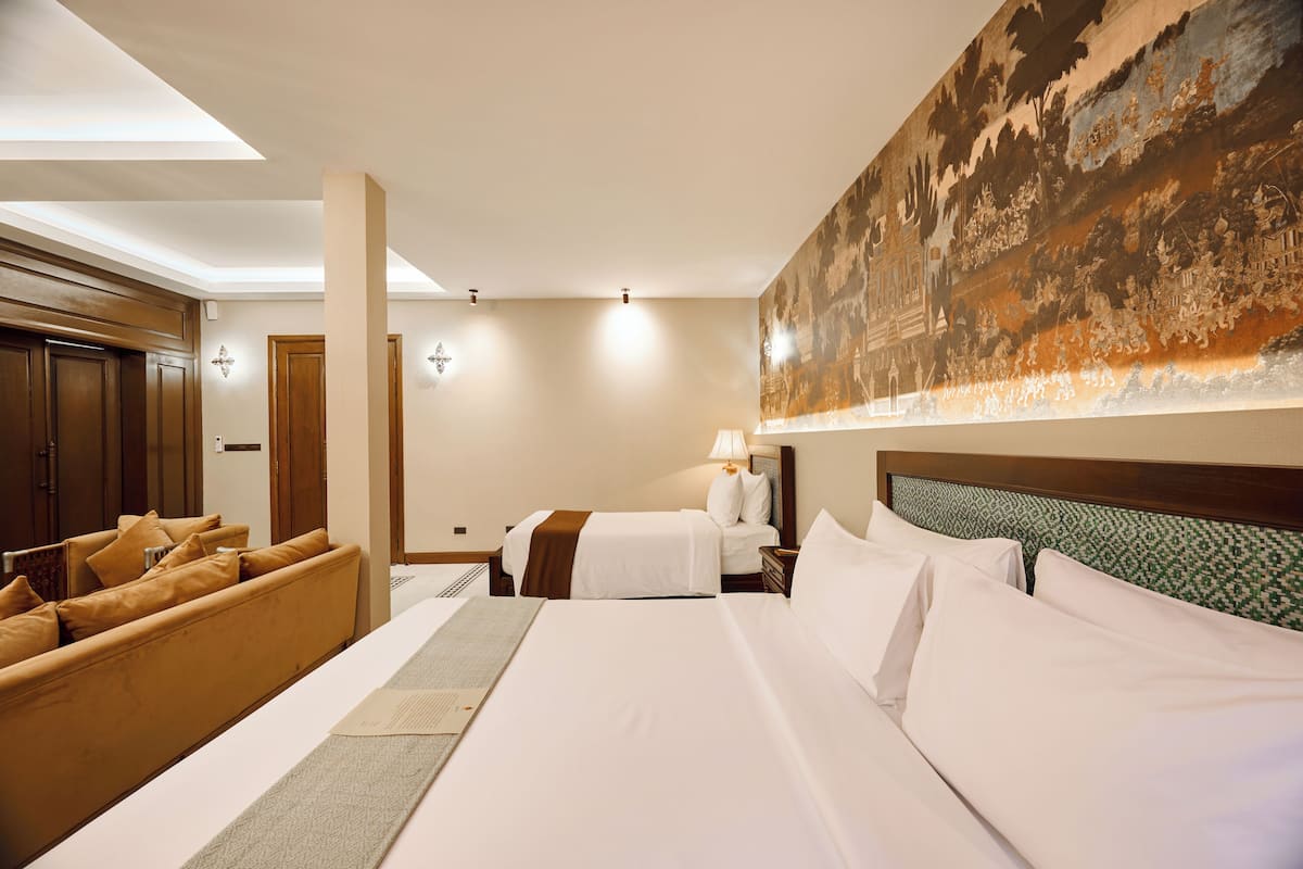 A hotel room with a large bed, a sofa, a desk, and a wall mural.