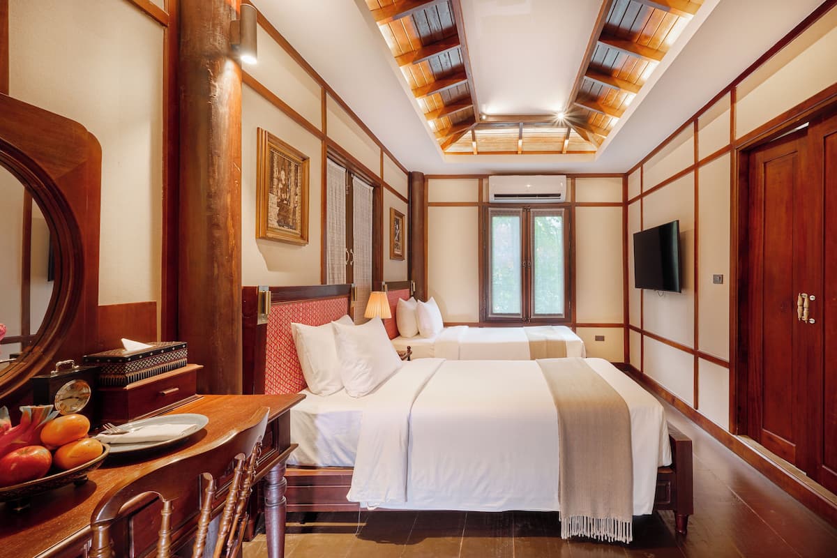 A hotel room with a large bed, a desk with a mirror, a TV, and a wooden ceiling.