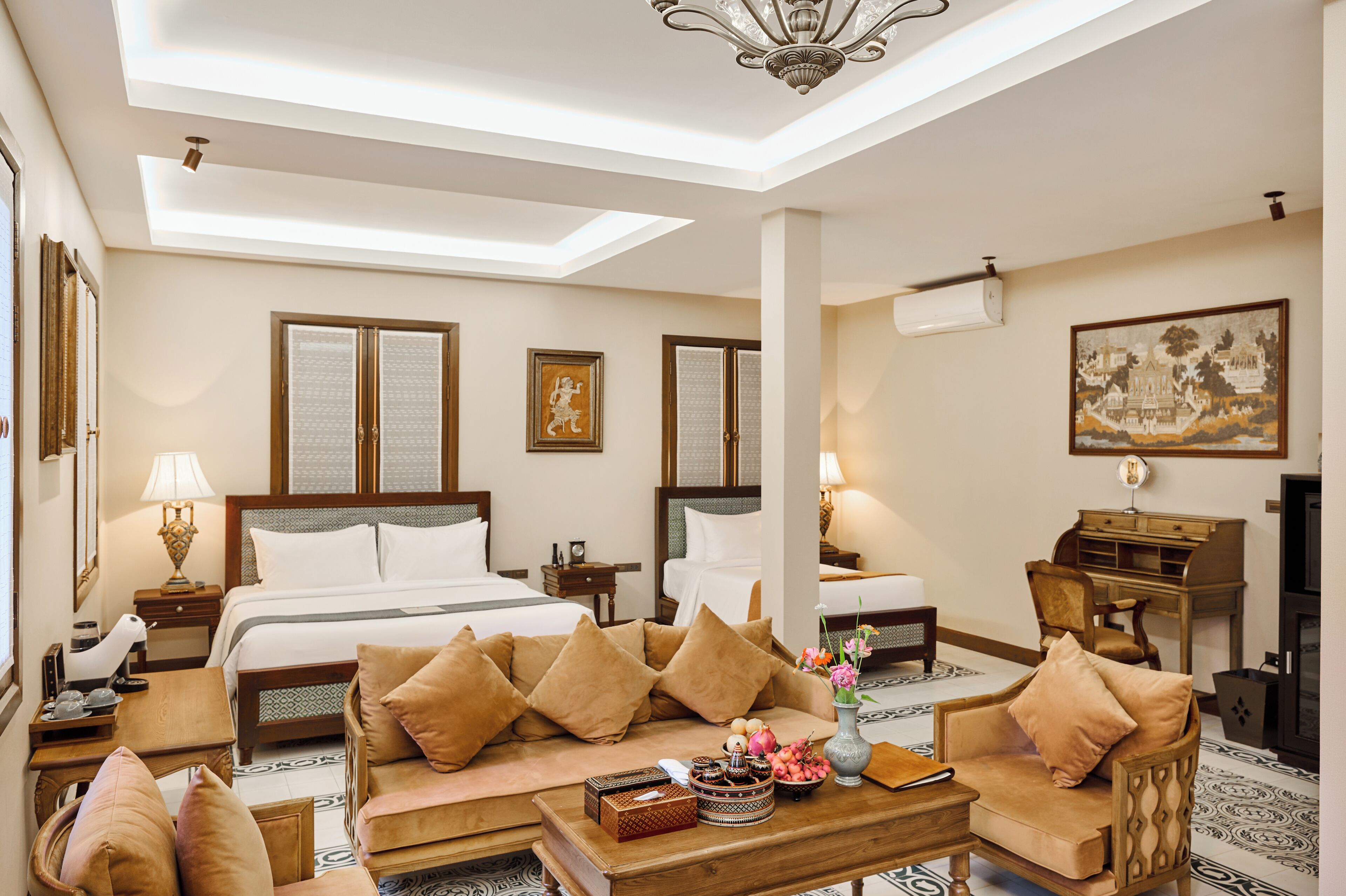 A hotel room with a large bed, two bedside tables, a sofa, a desk, and a chandelier.