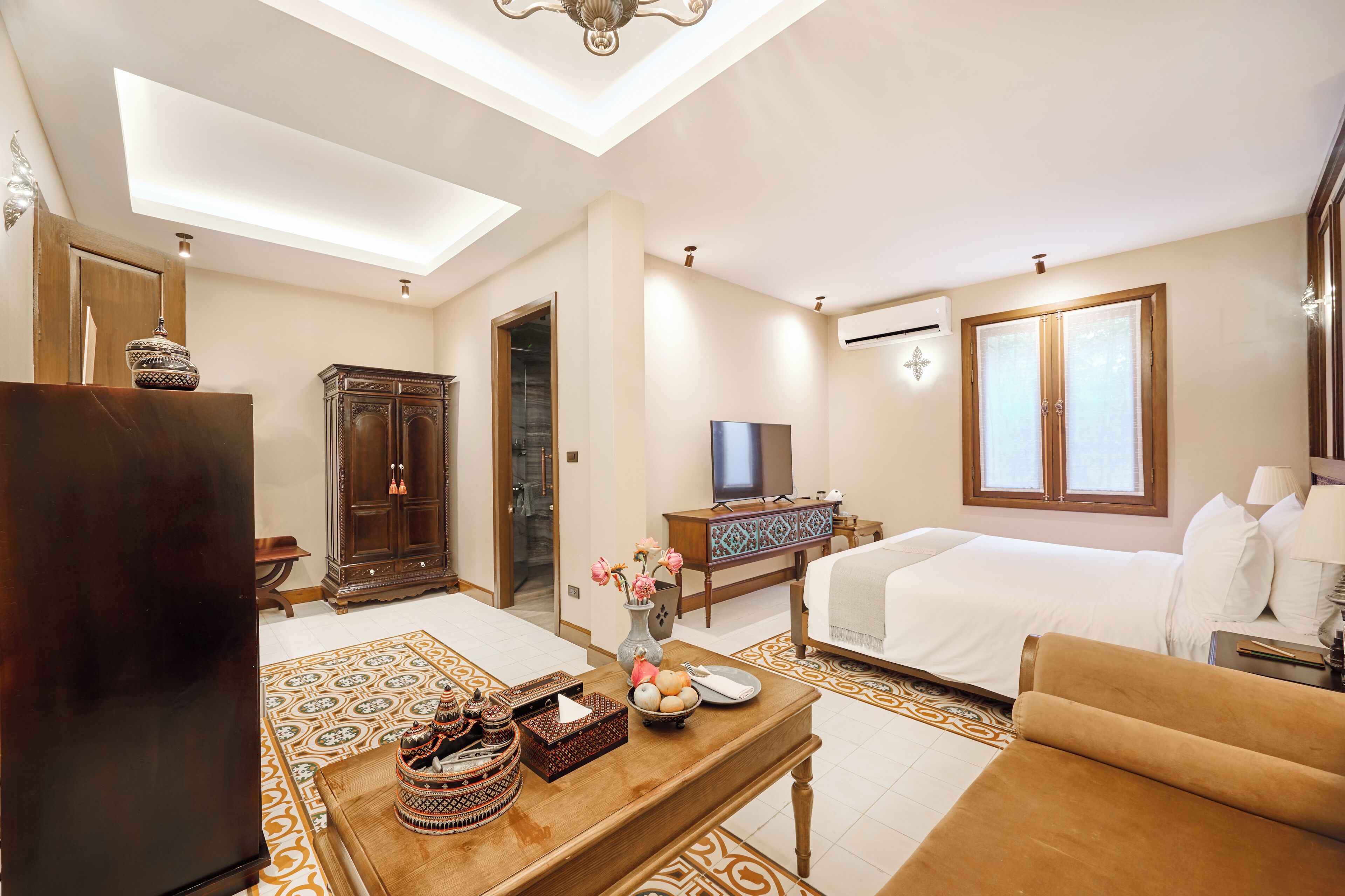 Habitación de hotel con cama, sofá, televisor, aparador de madera y una mesa de comedor con adornos.