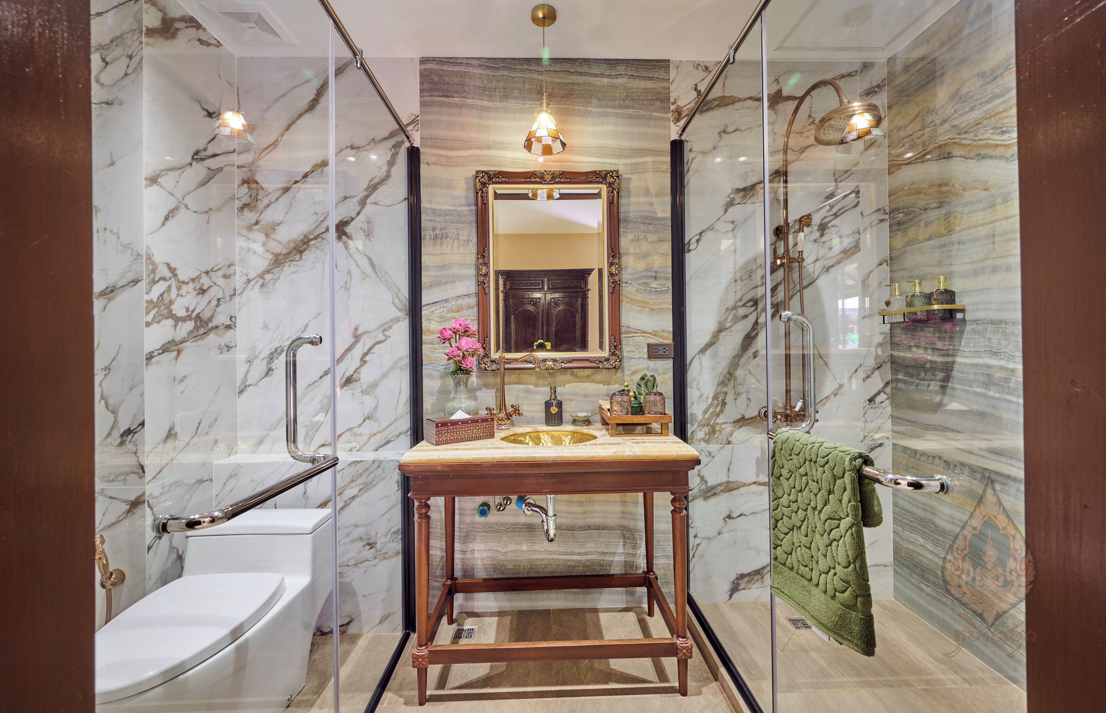 Un baño con pared de mármol, tocador de madera, lavamanos, inodoro y ducha.