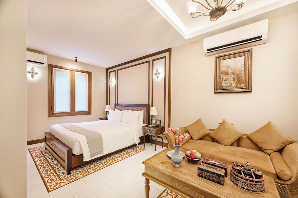 A hotel room with a bed, a sofa, a table with decorative items, an air conditioner, and a framed picture on the wall.