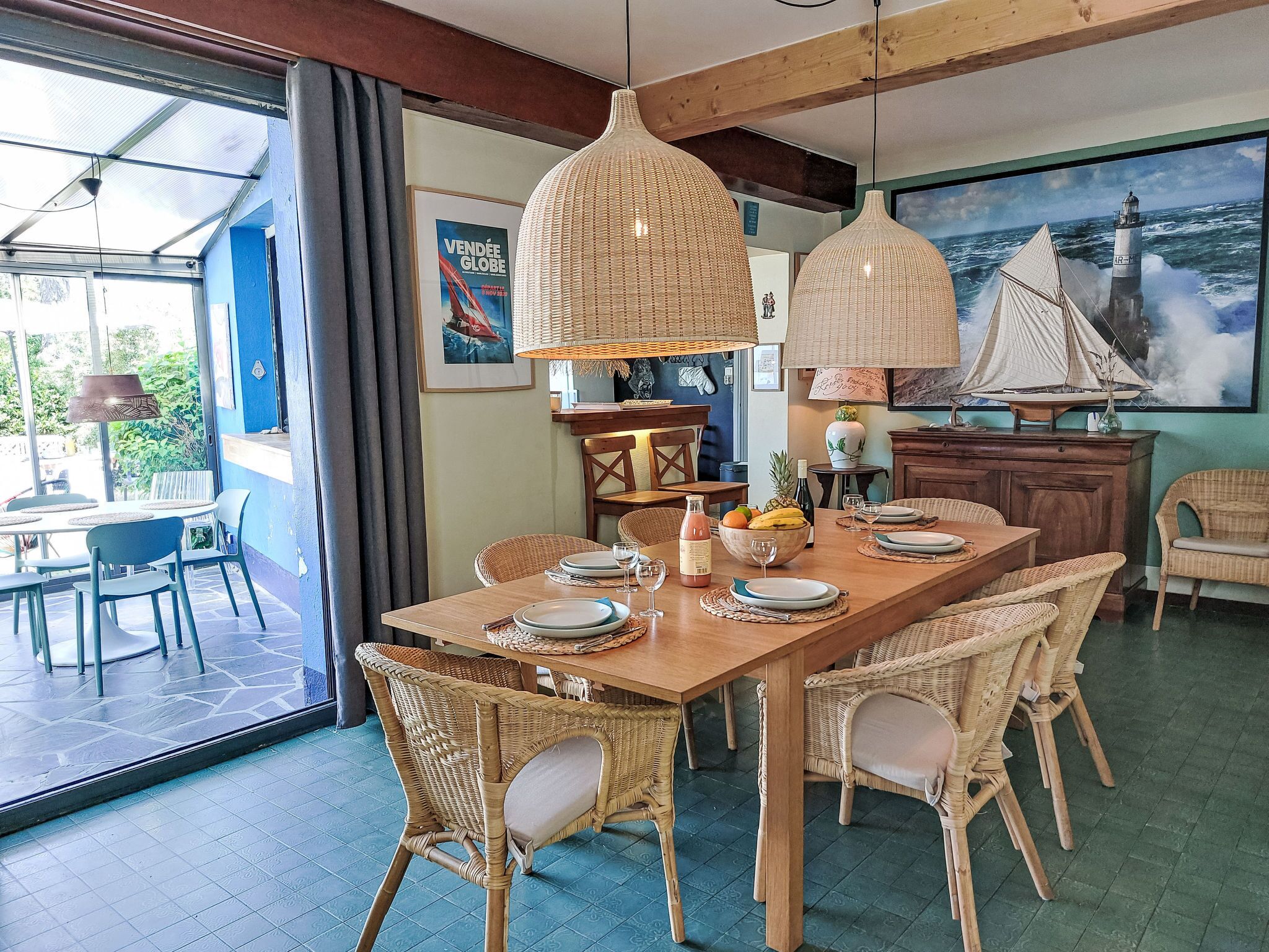 A dining area with a large wooden table, wicker chairs, and hanging pendant lights.