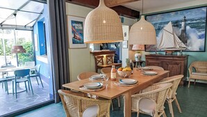 Un comedor con una gran mesa de madera, sillas de mimbre e iluminación colgante.