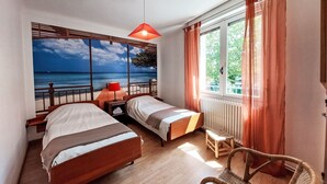 Un dormitorio con dos camas, vista al mar, una lámpara roja y una silla de mimbre.