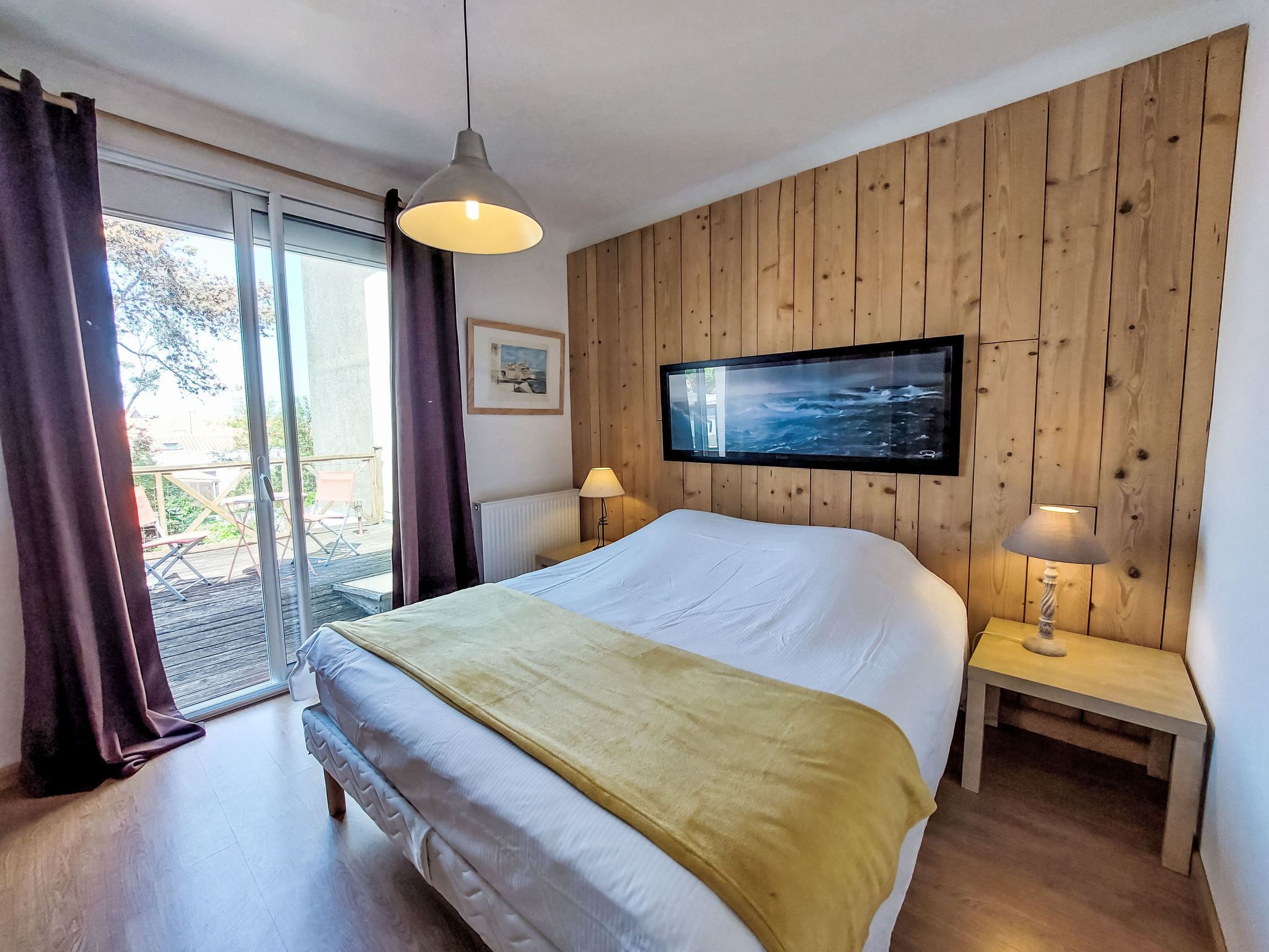 A bedroom with a bed, a TV mounted on the wall, a window with curtains, and a wooden floor.