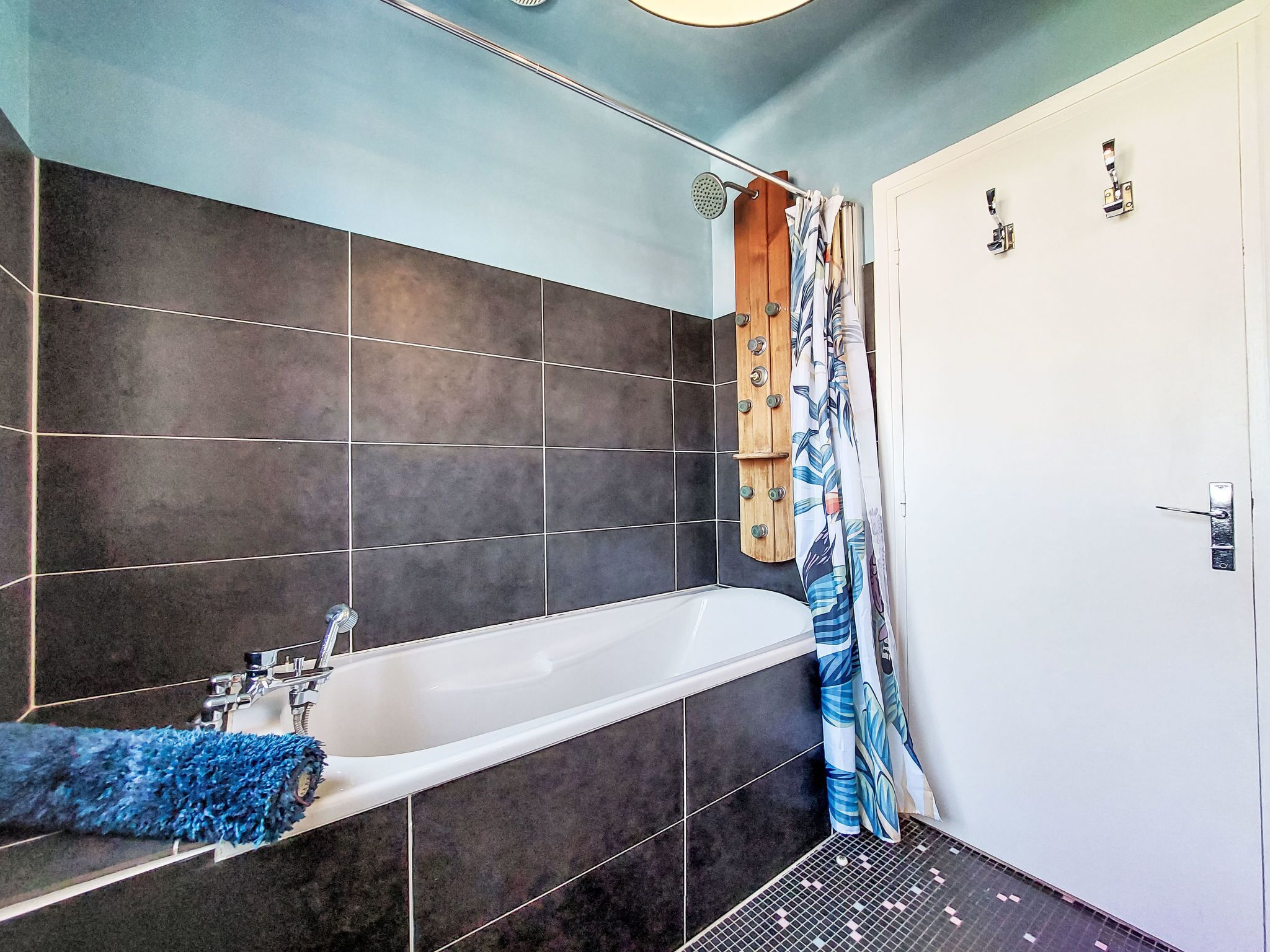 A bathroom with a bathtub, dark tiles, a shower curtain, and a door with a handle.