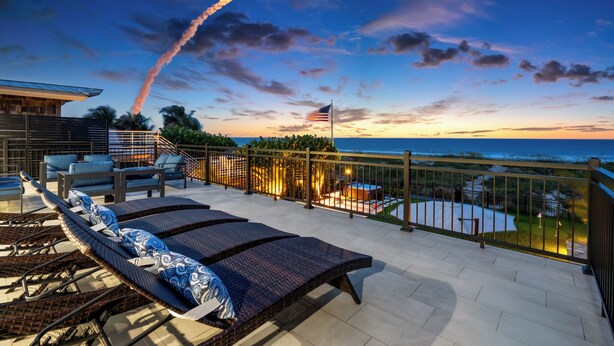 A rooftop terrace with lounge chairs, a flag, and a view of the ocean at sunset. - Oceanfront 6BDRM 4.5BA w/ Movie Rm, Game Rm, Hot Tub, Fire Pit, Summer Kitchen (Cocoa Beach)