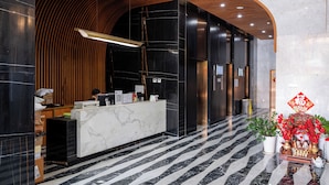 Un hall d’hôtel moderne avec un comptoir d’accueil en marbre, des panneaux muraux en bois et un sol à rayures noires et blanches.