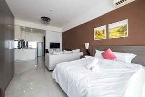 A modern hotel room with a large bed, a sofa, a TV, and a kitchen area visible through an open door. - Yue Tai Apartment City Center by Soben (Phnom Penh)