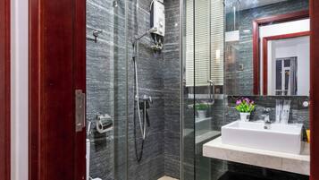 Un baño moderno con cabina de ducha de vidrio, un lavamanos blanco y un salpicadero de mármol.