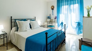 A bedroom with a bed, a bedside table, a dresser, a chair, and a window with curtains.