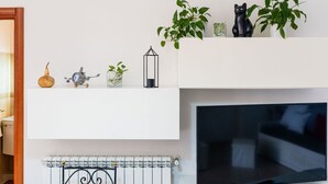 A living room with a flat-screen TV, a white fireplace, and decorative items on shelves.