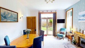 A cozy living room with a wooden dining table, blue chairs, a fireplace, and a large window with curtains.