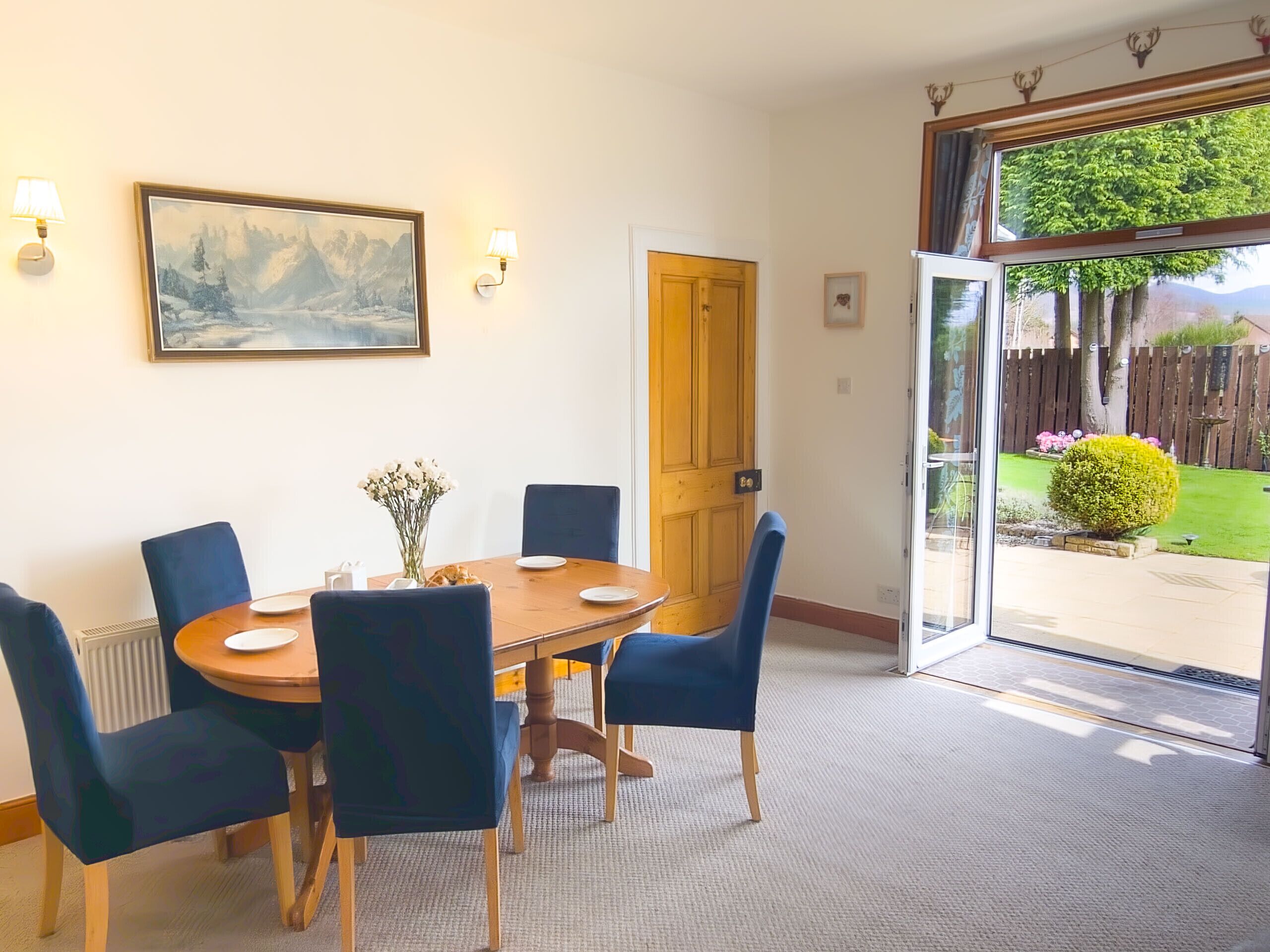Un comedor con una mesa de madera, sillas azules, un jarrón con flores y un cuadro en la pared.