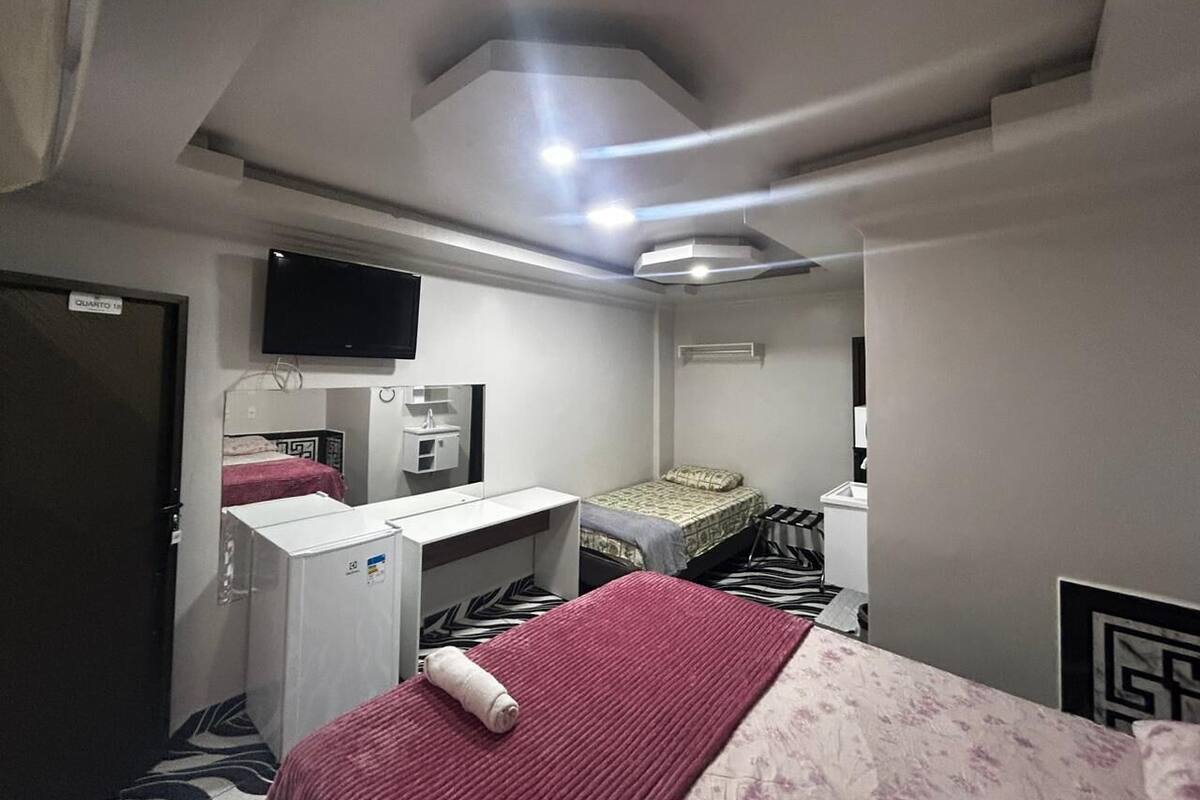 A compact hotel room with a bed, a desk, a television, and a small kitchenette.