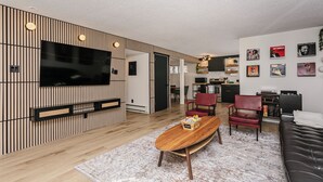 A modern living room with a flat-screen TV, a wooden coffee table, red chairs, and a black sofa. - Cozy Retro Gem for the Fam W/ AC (Near Roger&WEM) (Edmonton)
