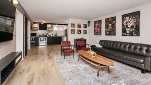 A modern living room with a black leather sofa, red chairs, a wooden coffee table, and a kitchen in the background. - Cozy Retro Gem for the Fam W/ AC (Near Roger&WEM) (Edmonton)