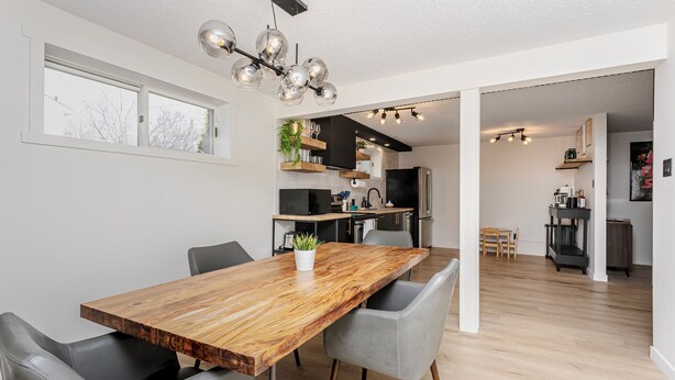 A modern kitchen with a wooden dining table, grey chairs, and a hanging light fixture. - Cozy Retro Gem for the Fam W/ AC (Near Roger&WEM) (Edmonton)