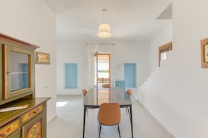 Un coin repas avec une table en verre, des chaises, un luminaire au plafond et une vue par la fenêtre.