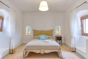 Une chambre à coucher avec un lit, des rideaux, un luminaire suspendu, deux tables de chevet et une fenêtre.