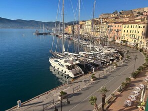 A marina with multiple sailboats docked, a waterfront promenade with outdoor seating, and colorful buildings in the background. - With a view of the Darsena of Portoferraio (Portoferraio)