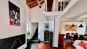 Un vaste espace de vie agrémenté d’une cheminée, un coin repas avec une table et des chaises, et un escalier menant à l’étage supérieur.