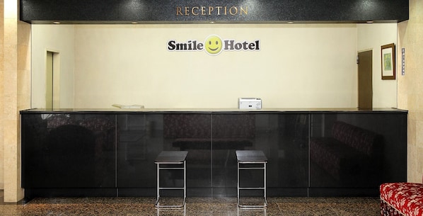 Un mostrador de recepción con un letrero que dice 'Smile Hotel', dos taburetes negros y un cuadro en la pared.