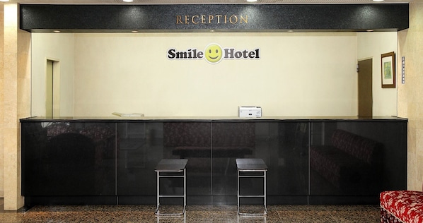 A reception desk with a 'Smile Hotel' sign, two black bar stools, and a framed picture on the wall.