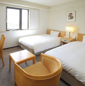 A hotel room with two beds, a desk, a chair, and a window.
