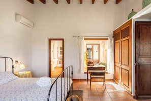 A bedroom with a bed, bedside lamp, and a view of a dining area through an open door.