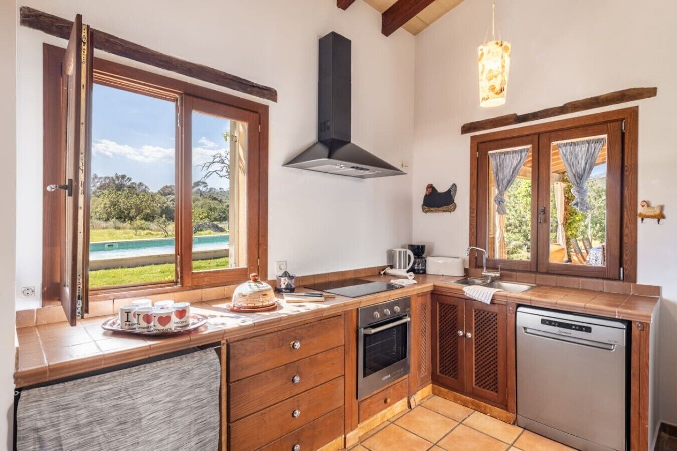 A kitchen with wooden cabinets, a stove, a dishwasher, and a window overlooking a pool.