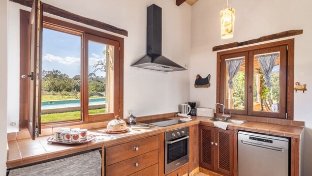 Una cucina con mobili in legno, un piano cottura, una lavastoviglie e una finestra con vista su una piscina.