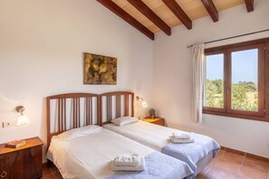 Un dormitorio con dos camas, una ventana con cortinas, un cuadro en la pared y una lámpara de noche.