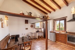 Una cocina rústica con vigas de madera, un comedor con banco y un ventanal que proporciona luz natural.