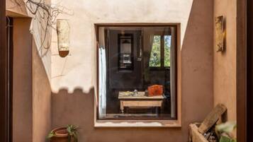 A narrow courtyard with a window, a wooden bench, and potted plants.