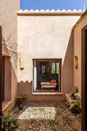 A narrow courtyard with a window, a wooden bench, and potted plants.