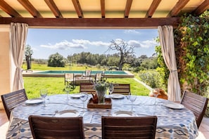 An outdoor dining area with a table set for four, overlooking a pool and garden.