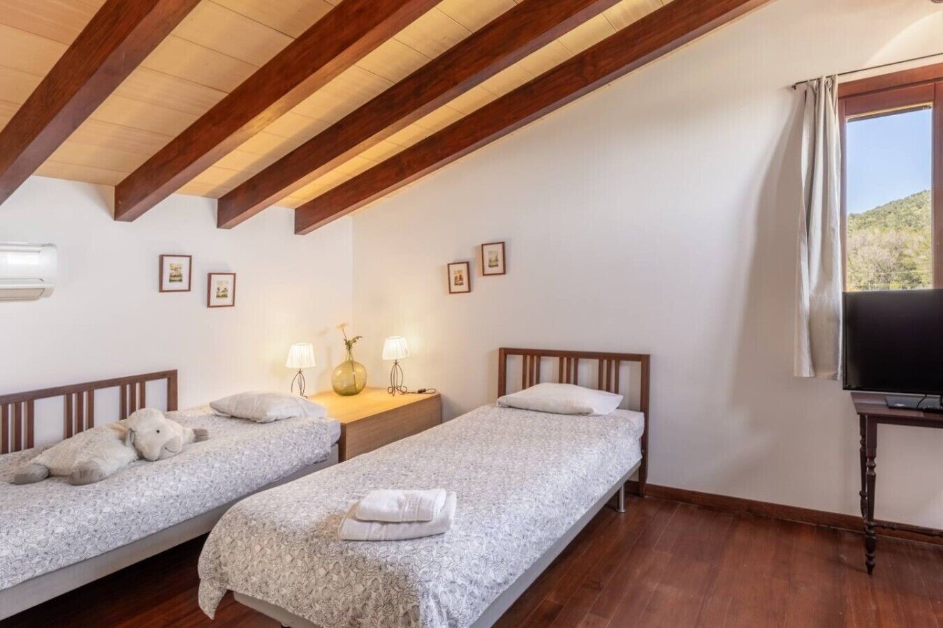 A bedroom with two single beds, a nightstand with lamps, a TV, and a window with curtains.