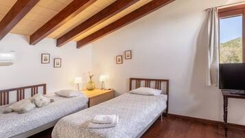 A bedroom with two single beds, a nightstand with lamps, a TV, and a window with curtains.