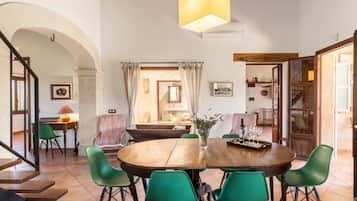 A dining area with a round wooden table, green chairs, and a hanging light fixture.