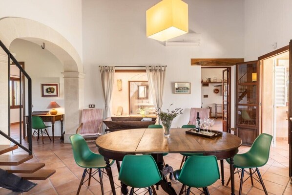 A dining area with a round wooden table, green chairs, and a hanging light fixture.
