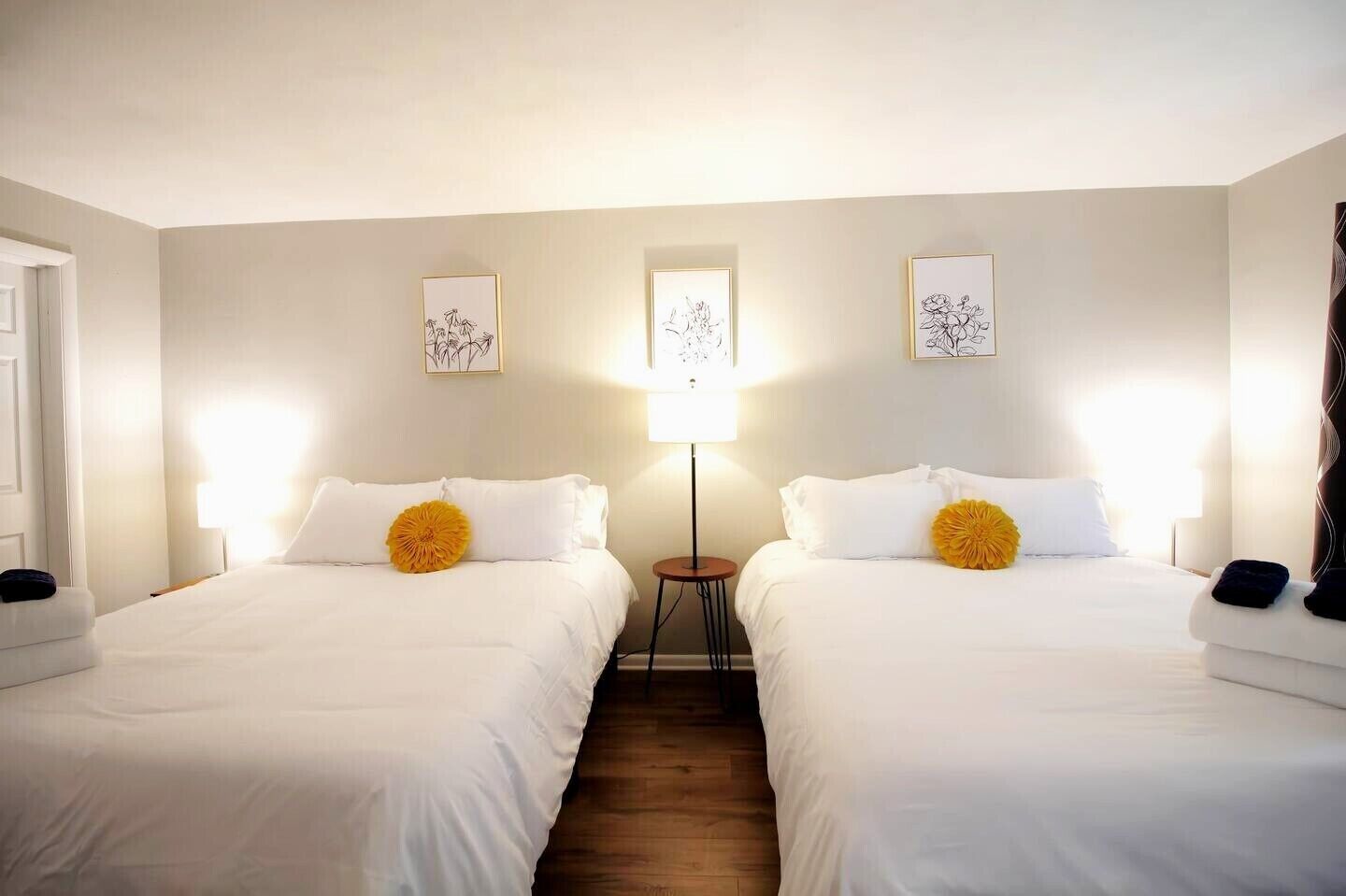 A hotel room with two single beds, a small table, and a lamp between the beds.