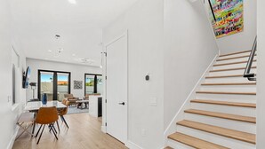 Un intérieur moderne avec un escalier, un plancher en bois et un coin repas comprenant des chaises et une table.