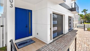 Un bâtiment moderne avec une porte bleue, portant le numéro 103, et un petit espace extérieur agrémenté d’un banc.