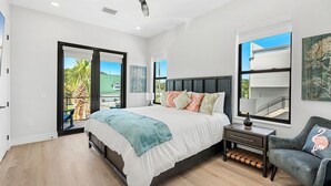 Une chambre à coucher moderne, équipée d’un lit, d’une table de chevet, d’une chaise, d’un ventilateur de plafond et d’une grande fenêtre donnant sur l’extérieur.