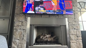 Una chimenea de piedra con un televisor de pantalla plana montado encima, mostrando un partido de baloncesto.