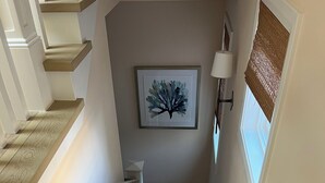 Una escalera de madera con barandilla, una obra de arte enmarcada en la pared y una ventana con persiana.
