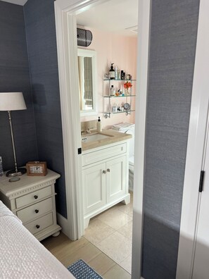 A bathroom with a white vanity, a mirror, a shelf with toiletries, and a clock.