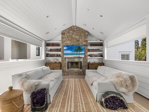 A modern living room with white walls, a stone fireplace, and bookshelves filled with books.